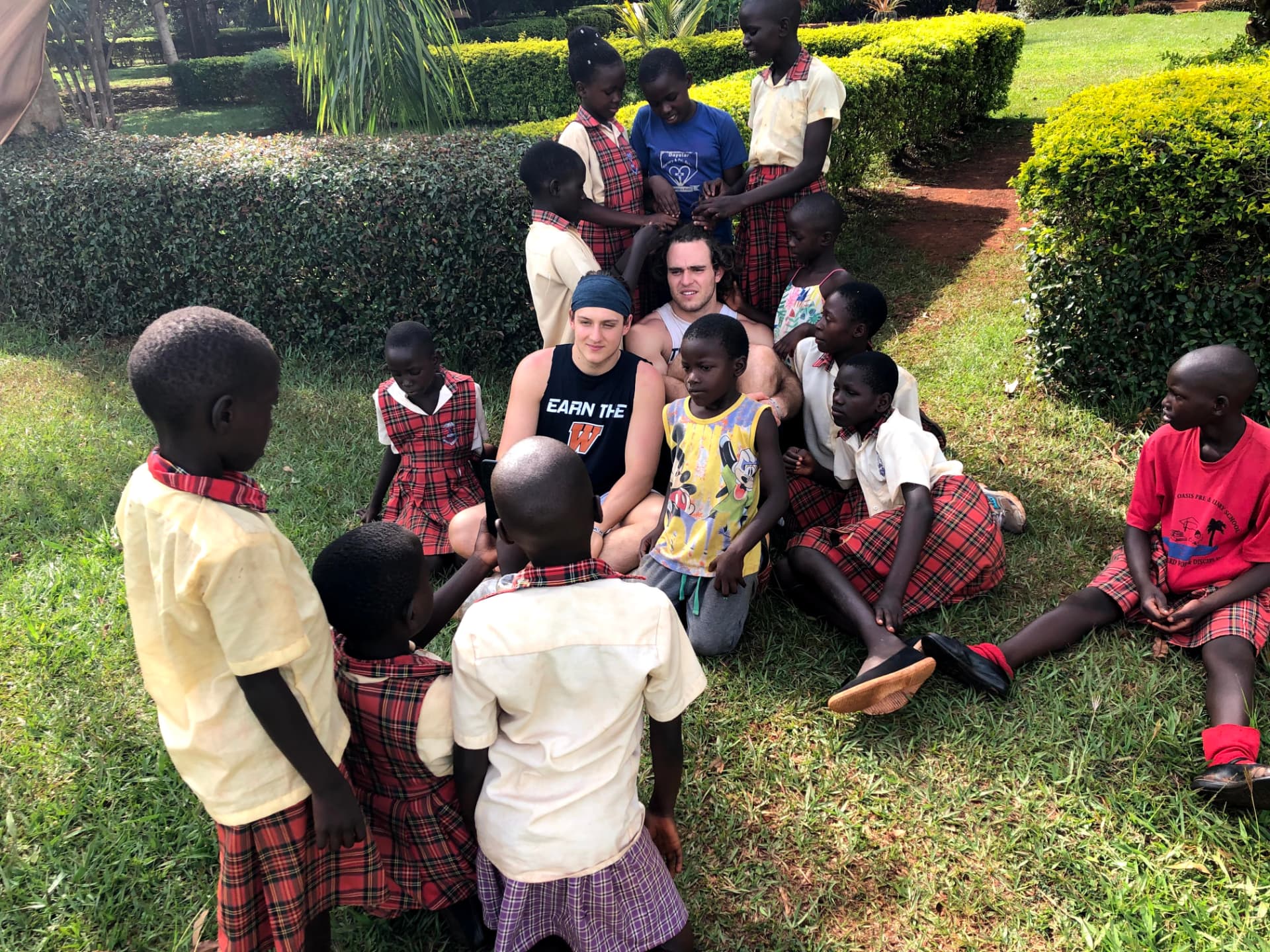 Two team members sitting in the grass talking with a group of schoolchildren