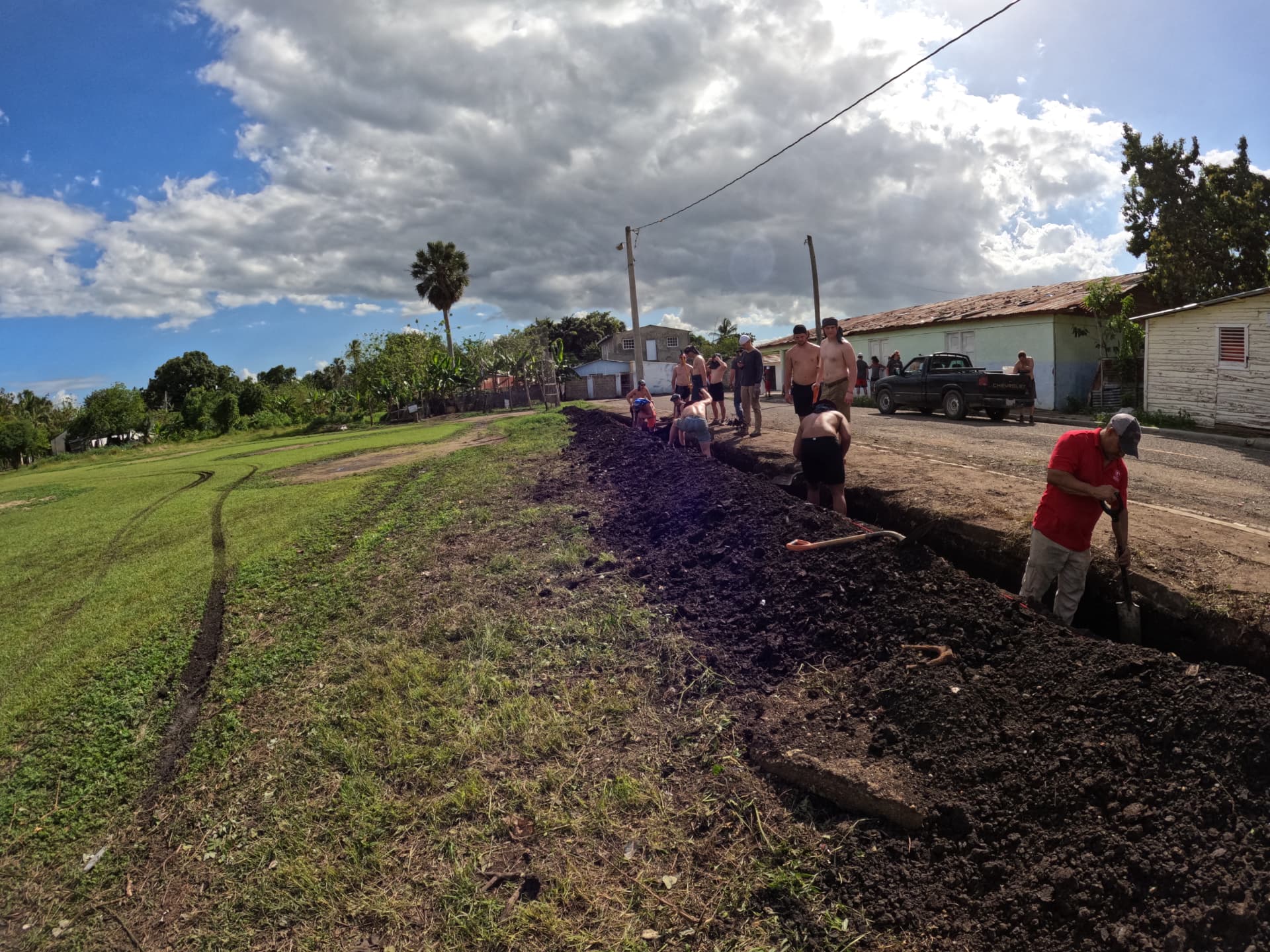 Team digging a long trench alongside a village road