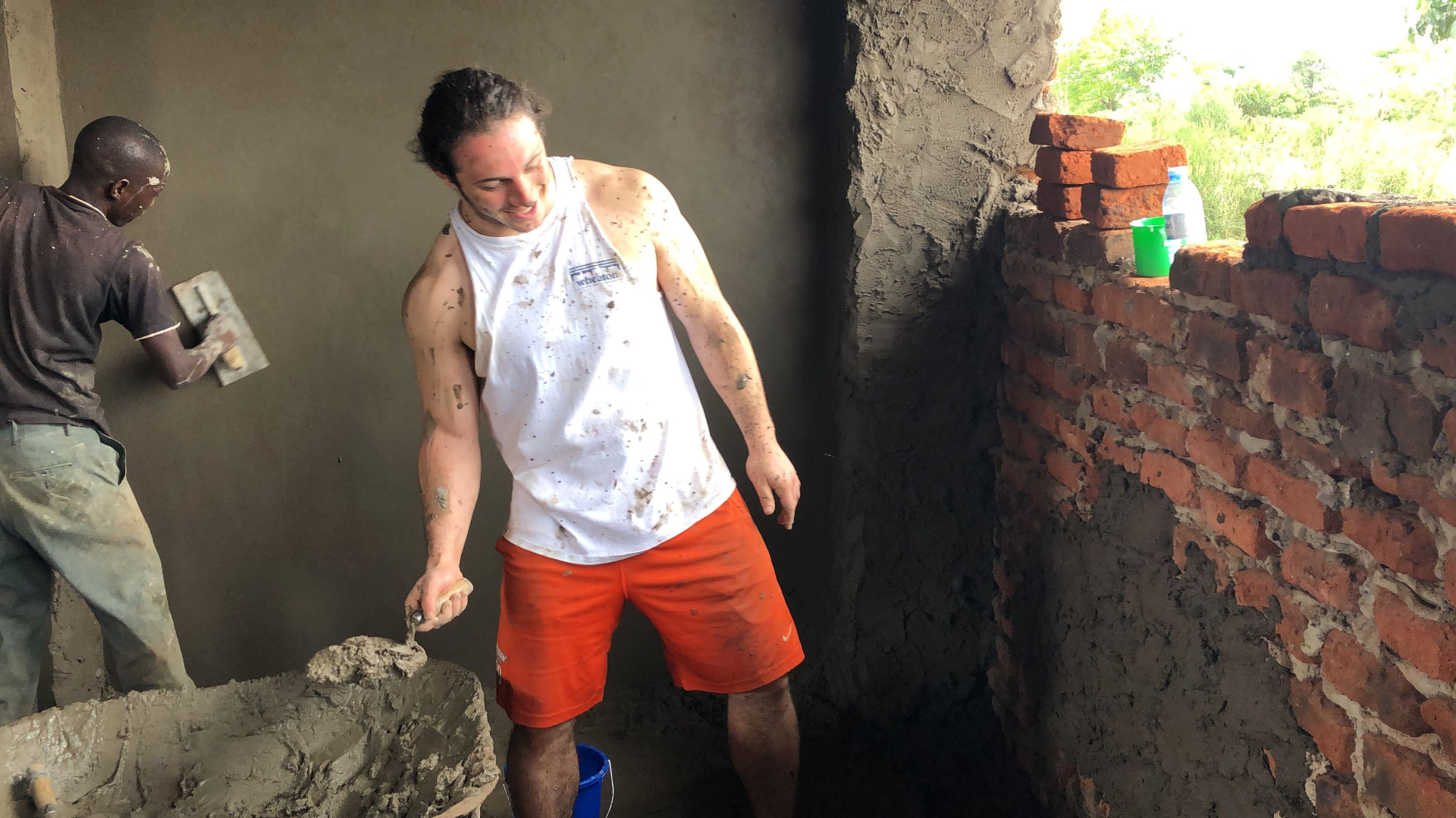 An athlete mixing and spreading mortar alongside a local mason