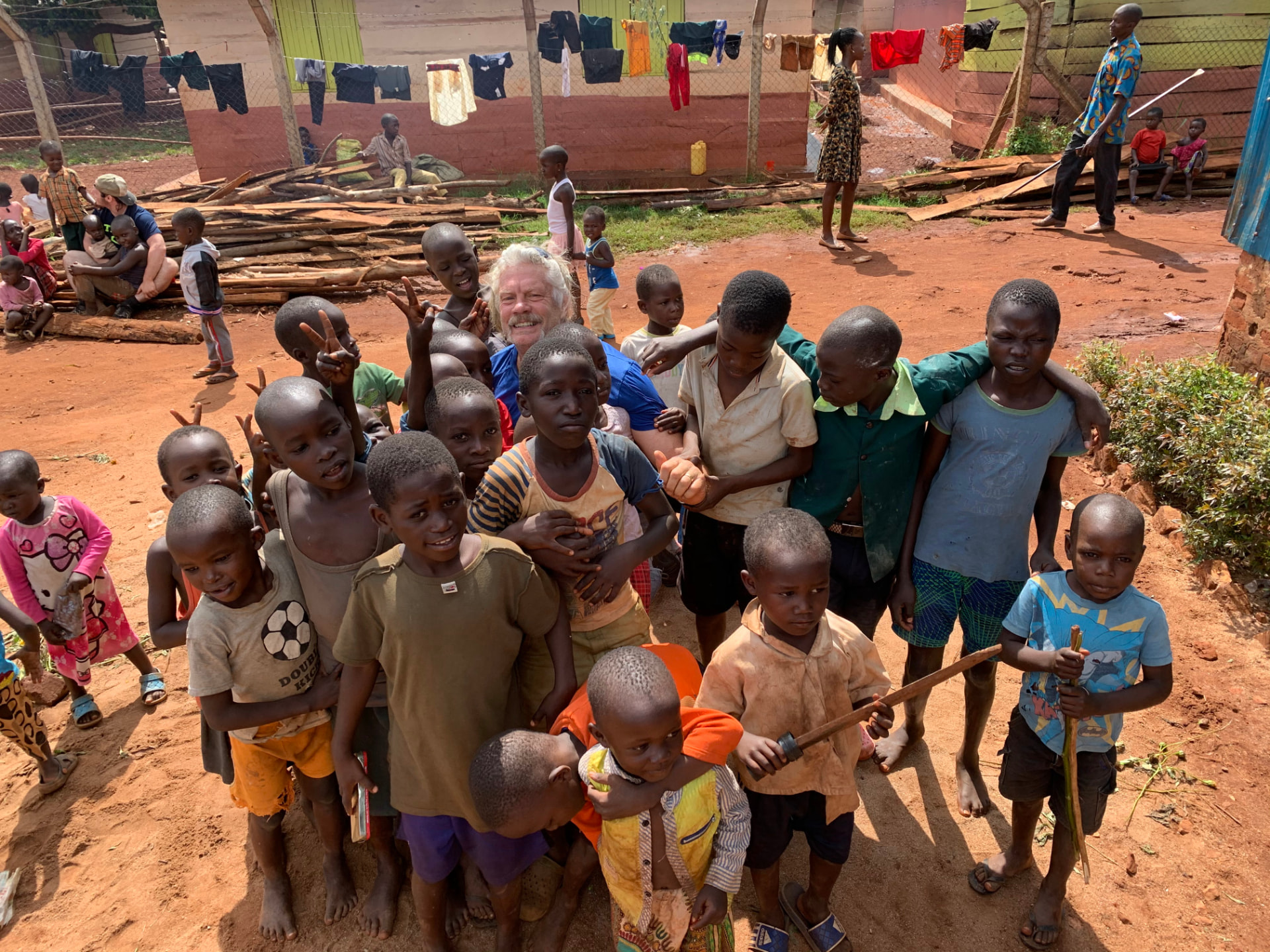 A crowd of smiling children surrounding a team member in a village courtyard