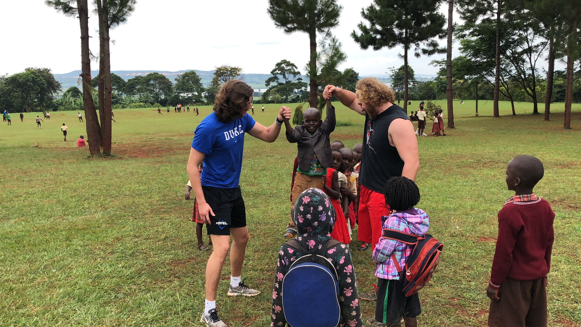 Two athletes lifting a young boy by the hands on an open field
