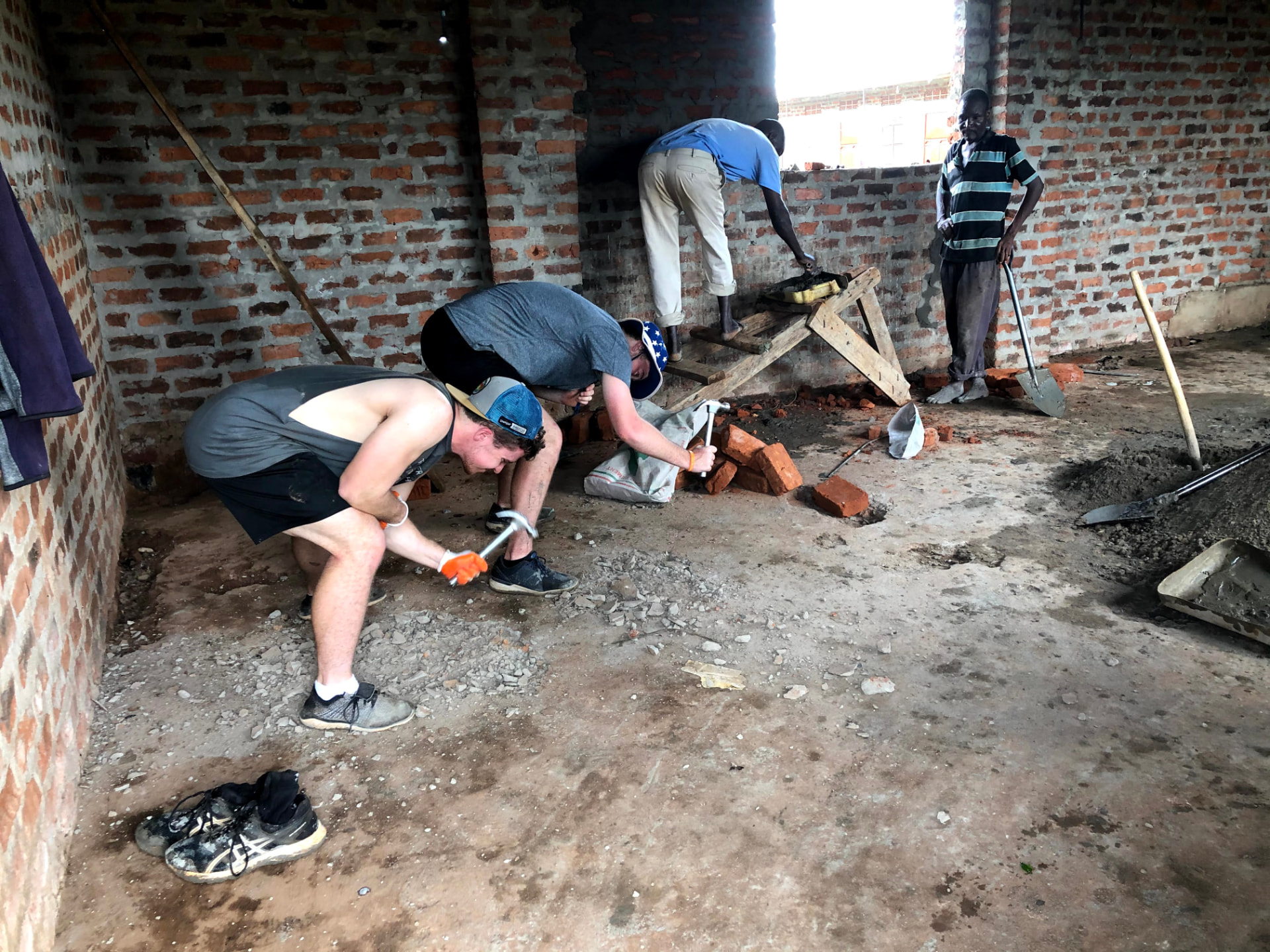 Team members breaking ground and hauling brick inside an unfinished building