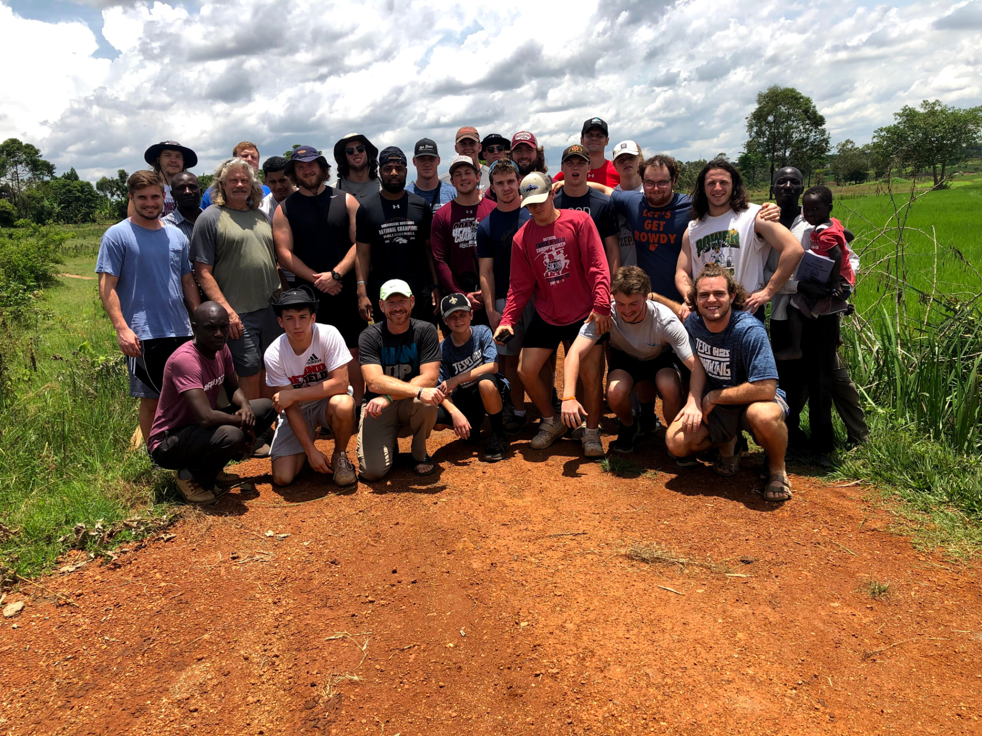 The full mission team gathered on a red dirt road beside green fields
